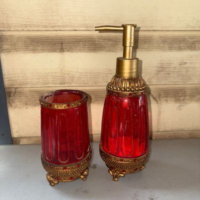 Sale Photo Thumbnail #336: A 2-piece vanity or bathroom set featuring a lotion/soap dispenser and matching tumbler cup. Made of fluted red glass with ornate antique-gold tone metal/resin bases and rims, accented with faux red rhinestones. Includes ornate footed bases. Shows light w