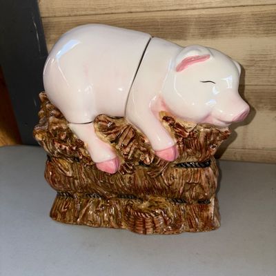 Sale Photo Thumbnail #49: 8X8X5in.
A vintage glazed ceramic cookie jar shaped like a pink pig sleeping on top of a brown haystack base. Features a two-piece design where the top of the pig lifts off as a lid. Appears to be in good condition with minor surface wear consistent with 