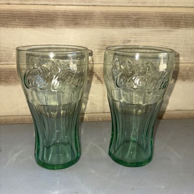 Sale Photo Thumbnail #215: A set of two green glass Coca-Cola contour tumbler glasses featuring embossed script lettering and fluted design. Both glasses appear to be in good condition with no visible chips or cracks.
6in tall