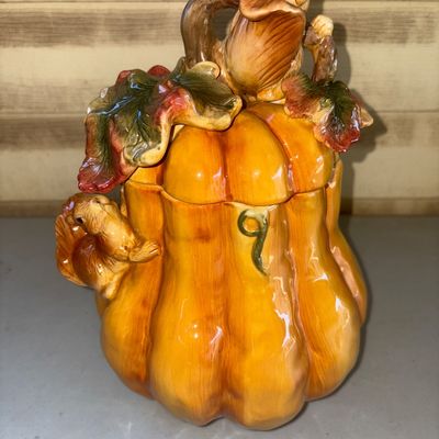 Sale Photo Thumbnail #157: Decorative ceramic pumpkin-shaped cookie jar or lidded canister featuring molded squirrels, autumn leaves, and a stem handle on the lid. High-gloss glazed finish in warm yellow, orange, green, and brown tones. Includes removable lid. Excellent condition w