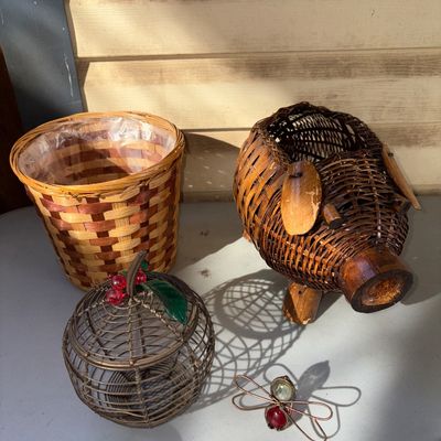 Sale Photo Thumbnail #341: A collection of 4 decorative home pieces featuring:
- A woven wicker pig-shaped planter or holder
- A round woven two-tone planter basket with plastic lining
- An apple-shaped metal wire basket with faux berries and leaf accent
- A small wire dragonfly or