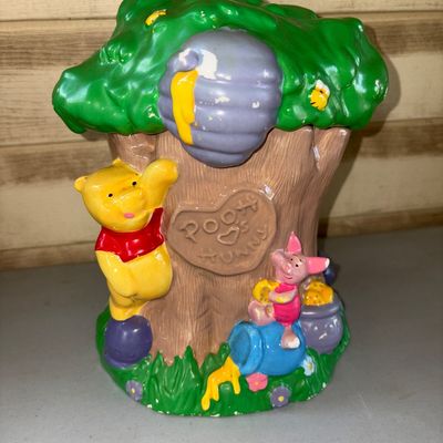 Sale Photo Thumbnail #50: 10X5in
Vintage ceramic cookie jar featuring Disney's Winnie the Pooh and Piglet around a tree trunk with a beehive lid inscribed 'Pooh's Hunny'. Shows some paint wear and minor scuffs, particularly on the beehive section of the lid, but overall in good us