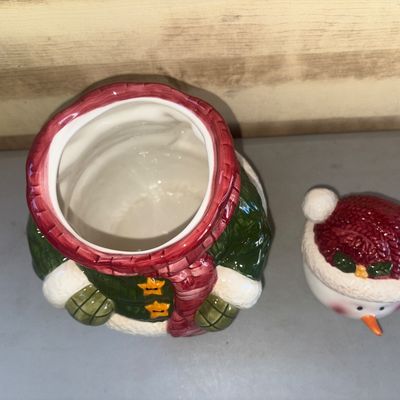Sale Photo Thumbnail #255: A festive ceramic snowman cookie jar featuring a green jacket, red scarf, winter hat, and star buttons. Clean interior, overall good condition with no visible cracks or chips.
11in tall