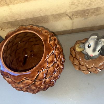 Sale Photo Thumbnail #261: A charming vintage ceramic cookie jar designed as a brown pinecone, featuring a removable lid topped with a grey squirrel figurine holding an acorn. High-gloss glazed finish throughout. Appears to be in good vintage condition with no major chips or cracks