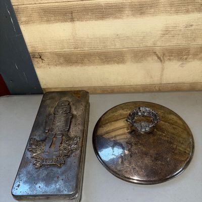 Sale Photo Thumbnail #222: Lot includes a vintage rectangular metal tin dated 1997 with an embossed nutcracker design on the lid, along with a round silver-tone metal lid featuring an ornate decorative handle. Both items show signs of age including surface oxidation, tarnishing, ru
