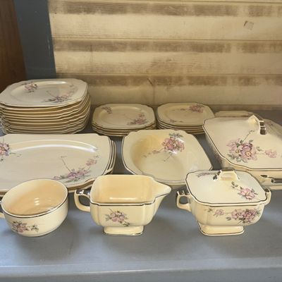 Sale Photo Thumbnail #280: Comprehensive vintage ceramic/china dinnerware service featuring a cream-colored base with delicate pink floral motifs and metallic trim accenting the scalloped edges. Includes a large covered casserole/tureen, covered sugar bowl, creamer, open vegetable 