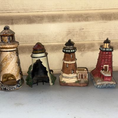 Sale Photo Thumbnail #361: Collection of four miniature lighthouse figurines crafted from resin and ceramic materials. Includes detailed architectural designs depicting various lighthouse styles. Condition varies; one figurine has notable damage/breakage to the front shell. Please 