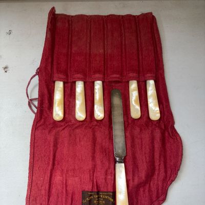 Sale Photo Thumbnail #335: Set of six antique flatware spreaders featuring mother of pearl handles and sterling silver ferrule details, housed in their original red cloth storage roll pouch labeled 'R. Wallace & Sons Mfg. Co., Wallingford, Conn.'. Light surface patina consistent wi