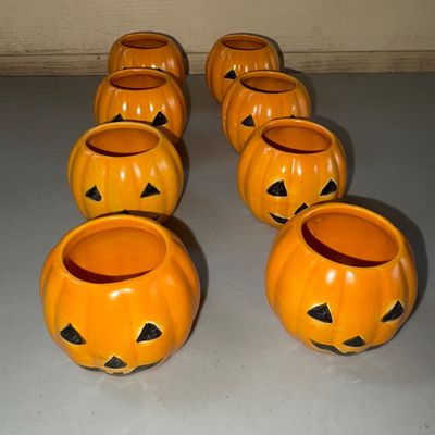 Sale Photo Thumbnail #74: Set of 8 orange ceramic jack-o'-lantern shaped holders, suitable for tealights, votive candles, or small planters. Features classic black painted jack-o'-lantern faces with open tops. 

Condition: Seven items are in good pre-owned condition with light wea