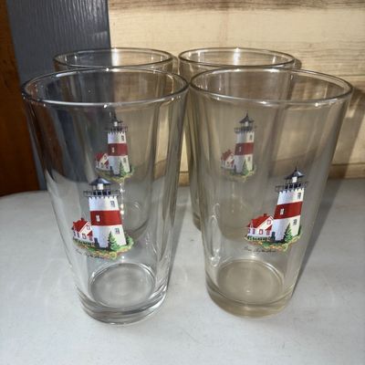 Sale Photo Thumbnail #308: Set of four clear glass pint tumblers featuring a red-and-white lighthouse motif with a small building at the base, signed by artist Pam Clayton Ward. Good used condition with no visible chips or cracks.
6in tall