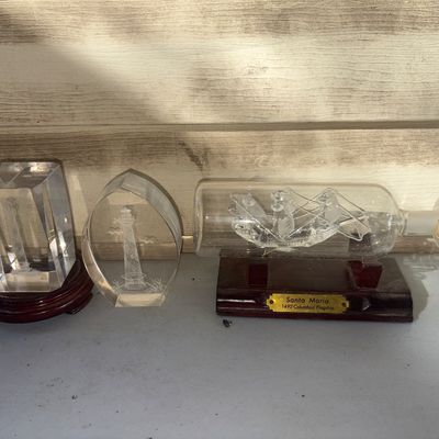 Sale Photo Thumbnail #345: Collection of three glass decorative items including a hand-blown glass ship in a bottle mounted on a wooden base labeled 'Santa Maria 1492 Columbus' Flagship' (note: glass rigging inside bottle appears broken/detached), alongside two laser-etched crystal