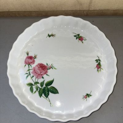Sale Photo Thumbnail #356: White ceramic or porcelain round quiche/tart baking dish featuring a scalloped edge and a central pink rose motif with smaller floral accents along the rim. Shows light surface wear consistent with age and minimal use; no chips or cracks visible in photos
