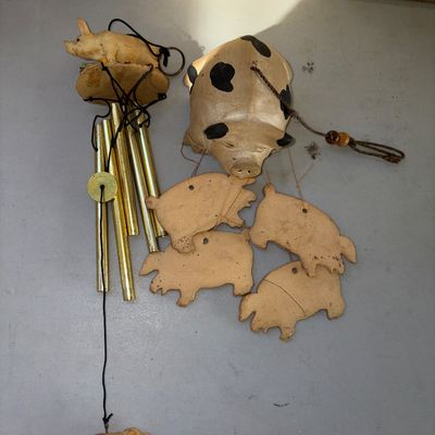 Sale Photo Thumbnail #340: Pair of novelty pig-themed wind chimes. Includes one metal chime set featuring resin pig figures and brass-tone metal tubes, and one ceramic spotted pig chime with hanging ceramic pig silhouettes. Both show light surface wear and minor scuffs, but appear 