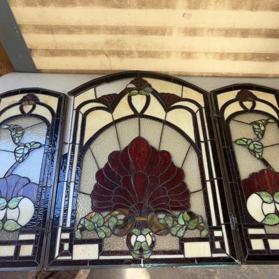 Sale Photo Thumbnail #326: A 3-panel hinged stained glass fireplace screen featuring an intricate Art Nouveau floral/fan pattern in shades of deep red, green, cream, and textured clear glass. Heavy leaded metal framework with hinges connecting the side panels to the central arched 