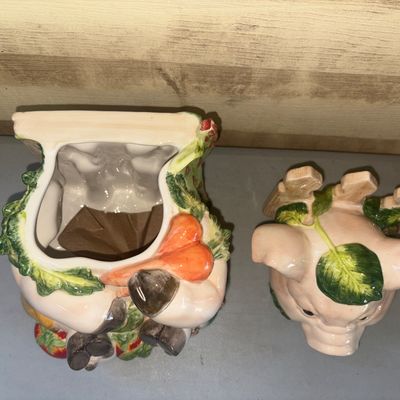 Sale Photo Thumbnail #259: Hand-painted ceramic cookie jar featuring a seated pig holding a carrot, surrounded by garden vegetables such as lettuce, tomatoes, and peas, with a picket fence detail on the back. The top section detaches as the lid. Glossy glazed finish. Shows light su