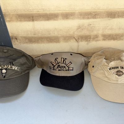 Sale Photo Thumbnail #224: A lot of three embroidered baseball caps/hats. Includes an olive green Mossberg hat with skull embroidery, a tan and black Tackle Box Ft. Smith, AR hat, and a tan Madison Trail hat with turtle embroidery. All show light wear consistent with pre-owned cond