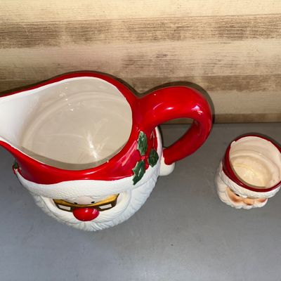 Sale Photo Thumbnail #162: A festive ceramic Santa Claus drinkware set featuring a large Santa face pitcher with glasses detail and a matching small Santa face mug. Made of glazed ceramic with hand-painted details. Condition: The pitcher appears in good pre-owned condition with vib