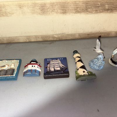Sale Photo Thumbnail #139: A collection of 6 nautical and maritime themed souvenirs and small decor items. Includes Texas Seaport Museum, Thomas Point Lighthouse, and Elissa 1877 magnets, along with a Cape Hatteras style lighthouse, seagull in flight figurine, and a small fisherman
