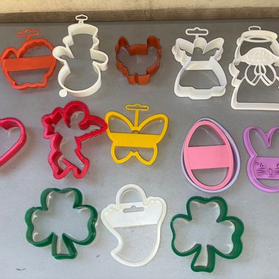 Sale Photo Thumbnail #268: Collection of 13 plastic cookie cutters featuring various holiday and seasonal shapes including shamrocks, angels, a snowman, turkey, Cupid, heart, butterfly, egg, bunny, and ghost. Includes brands like Wilton. Pre-owned condition with light signs of use.