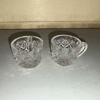 Sale Photo Thumbnail #209: Pair of clear pressed or cut glass cups featuring intricate diamond geometric patterns, textured handles, and starburst bases. Ideal for punch, tea, or decorative use. Both pieces appear to be in good condition with minor surface wear consistent with age 