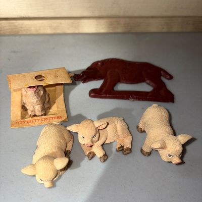 Sale Photo Thumbnail #65: Collection of small pig figurines, including three textured composite or plastic piglets, one tiny pig in original 'Itty Bitty Critters' cardboard packaging box, and a reddish-brown silhouette pig figure/cutout. Items show light wear consistent with age.