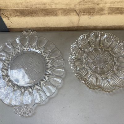 Sale Photo Thumbnail #287: Pair of clear pressed glass deviled egg serving platters. Includes one handled plate with molded egg wells and a central starburst/wheat pattern, and one scalloped tray with radial ribbed indents. Both items appear to be in good vintage condition with no 