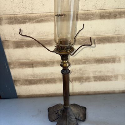 Sale Photo Thumbnail #396: Antique brass and cast iron adjustable lamp or shade stand base featuring a fluted column and a heavy metal leaf-form base with a turn key valve/switch. Includes a clear glass chimney shade with a ventilation ring and four brass shade support arms. Shows 
