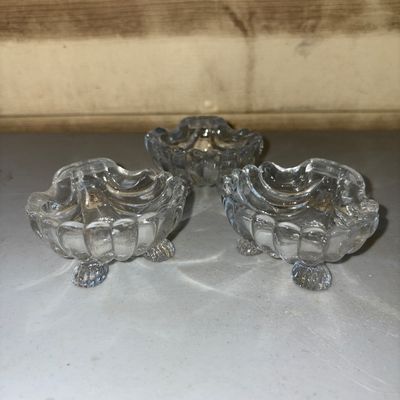 Sale Photo Thumbnail #212: A set of three matching vintage clear pressed glass open salt cellars or small trinket dishes. Designed in a scalloped sea shell shape with small ball feet underneath. Made of heavy pressed glass. All three pieces appear to be in good condition with no vi