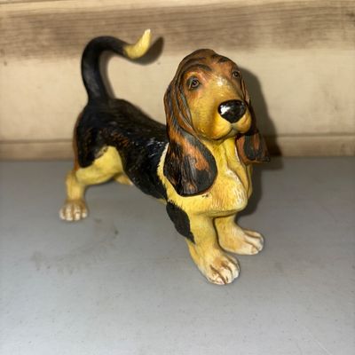Sale Photo Thumbnail #296: Hand-painted ceramic or resin figurine depicting a tri-color Basset Hound with long droopy ears and an upright tail. Shows minor wear and paint rubs consistent with age and display, but appears free of major cracks or chips.
4in tall