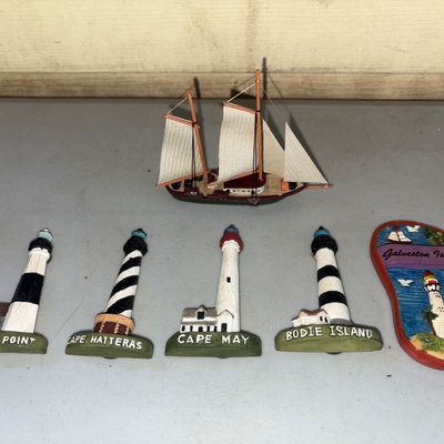 Sale Photo Thumbnail #140: A 6-piece lot of coastal and nautical souvenirs. Includes four dimensional lighthouse figures featuring Montauk Point, Cape Hatteras, Cape May, and Bodie Island; a Galveston Island flip-flop shaped souvenir magnet; and a miniature wooden model sailboat. I