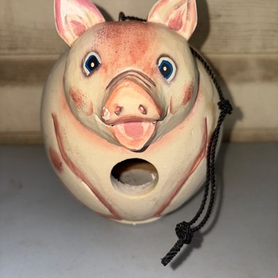 Sale Photo Thumbnail #297: Hand-painted ceramic or pottery birdhouse shaped like a round pig. Features a hanging cord attached at the top and a circular entry hole on the front. Shows light paint wear around the snout and ears, but remains intact with no major cracks visible.
7in t