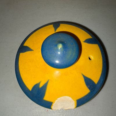 Sale Photo Thumbnail #220: Vibrant yellow ceramic pitcher or teapot featuring colorful hand-painted folk art illustrations including a figure with a pipe under a palm tree and a smiling sun motif. Bright blue glaze accents trim the spout, rim, lid, and handle. Note: There is a nota