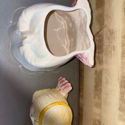 Sale Photo Thumbnail #167: Charming ceramic praying angel cookie jar with lid. Features pastel blue and white robes, blonde hair with a yellow halo, and pink feathered wings. Glazed finish. Shows light wear consistent with age, including subtle hairline cracking near the top rim of