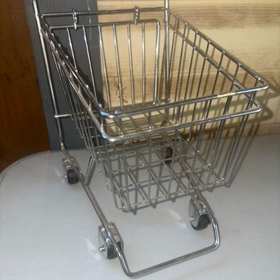 Sale Photo Thumbnail #240: Miniature wire shopping cart made of chrome-plated metal with rolling caster wheels and a coiled wire handle wrap. Suitable for use as a desktop accessory, novelty organizer, or decorative piece. Appears to be in good condition with light wear consistent 