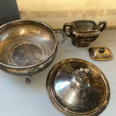 Sale Photo Thumbnail #266: A 2-piece collection of silver-plated serveware including a large footed covered tureen with ornate scroll handles and top finial, and a small dual-handled covered sugar bowl engraved with 'Cordelia'. Both pieces feature significant heavy tarnish, patina,