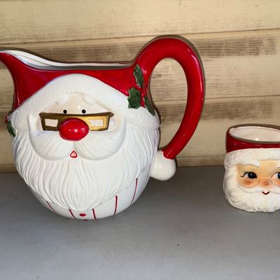 Sale Photo Thumbnail #161: A festive ceramic Santa Claus drinkware set featuring a large Santa face pitcher with glasses detail and a matching small Santa face mug. Made of glazed ceramic with hand-painted details. Condition: The pitcher appears in good pre-owned condition with vib