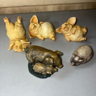Sale Photo Thumbnail #66: A collection of 5 small collectible pig figurines in various poses and styles, including three playful light-colored resin pigs, one sow with piglet figurine on a base, and one smooth stone or composite pig. All appear in good condition with minor light w