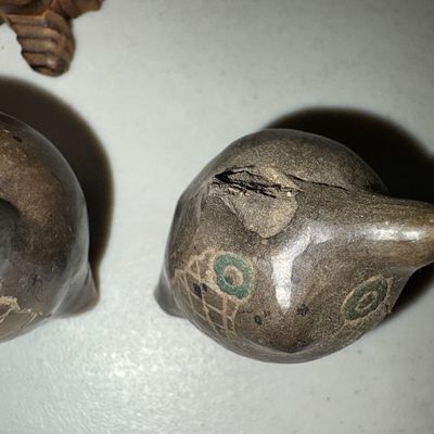 Sale Photo Thumbnail #18: A collection of four owl figurines crafted from various materials, including carved wood, molded resin/composite, and carved stone/soapstone. Set includes a detailed textured cream resin owl, a slender carved wooden owl with inset yellow glass eyes, and t