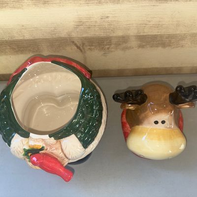 Sale Photo Thumbnail #253: Charming ceramic holiday cookie jar featuring a smiling moose wearing a green winter coat and red scarf, holding a red cardinal. Features a removable lid. High-gloss finish. Good overall condition with no visible cracks or major chips.
12in tall