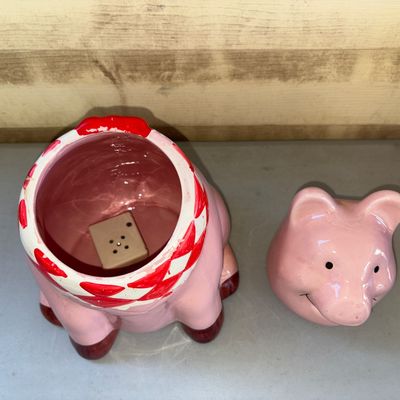 Sale Photo Thumbnail #194: Pink glazed ceramic pig cookie jar featuring a smiling face, red and white checkered neck scarf/bandana, and brown hooves. Removable head lid. Shows light wear to the paint around the neck area, otherwise appears in good condition with no visible cracks o