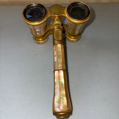 Sale Photo Thumbnail #5: Pair of antique brass opera glasses featuring iridescence mother of pearl / abalone panel inlay along the barrels and lorgnette handle. Features central focus adjustment wheel. Shows light vintage wear and tarnish to brass components consistent with age.