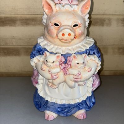 Sale Photo Thumbnail #191: Charming ceramic cookie jar featuring a mother pig in a blue dress and bonnet holding two piglets with pink bows. The removable lid forms the mother pig's head. Glazed finish with light overall crazing consistent with age, minor paint wear, but no visible