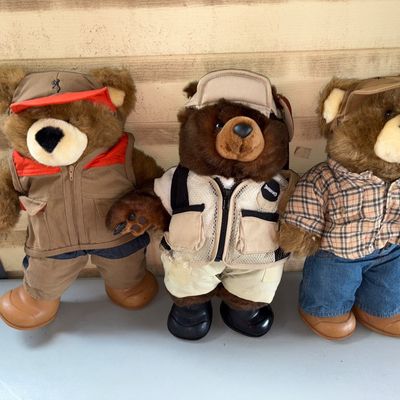 Sale Photo Thumbnail #94: Set of three plush teddy bears dressed in outdoor sports attire. Includes bears wearing a hunting vest with hat and boots, a fishing vest with hat, and a plaid shirt with jeans. Features Browning brand logos on select outfits. Items show minor wear consis