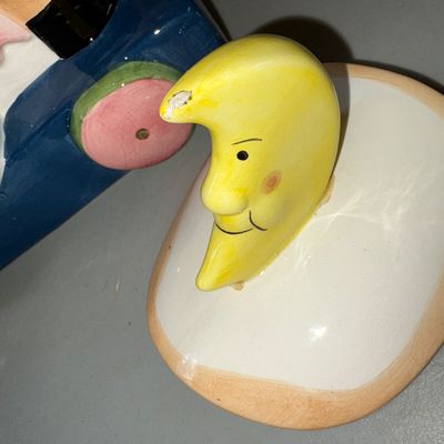 Sale Photo Thumbnail #86: Charming hand-painted ceramic cookie jar featuring a cow on a pull-toy style base with a cat, milk pail detail, and a crescent moon lid handle inspired by the nursery rhyme. Shows minor paint wear and small chips on the moon handle tip and horn.
10X8X10in