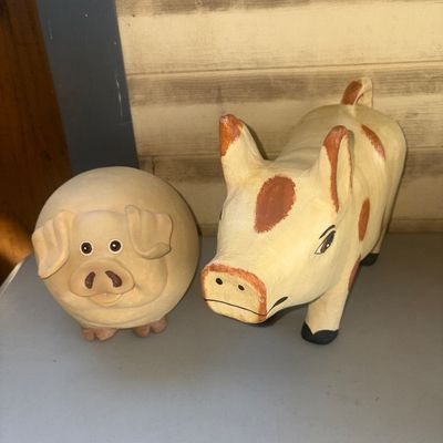 Sale Photo Thumbnail #263: Pair of decorative pig figurines featuring one rounded ceramic or clay pig with floppy ears and one painted wooden standing pig with spots. Both show light paint wear consistent with display use, with no major chips or cracks visible.
8in tall on right on