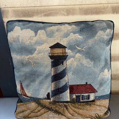 Sale Photo Thumbnail #386: Square decorative throw pillow with a woven tapestry front featuring a coastal lighthouse, sailboat, sand dunes, and seagulls. Finished with dark blue piping around the edges. Good pre-owned condition with minor signs of wear.
16X15in