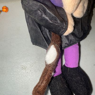 Sale Photo Thumbnail #367: A set of 3 Halloween decor items featuring a plush witch figurine holding a broom, a shelf-sitter pumpkin figure with leaf-style dangling legs, and a small decorative pumpkin stake accent with wire and beads. Items show minor wear, dust, and lint consiste