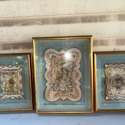 Sale Photo Thumbnail #391: A set of three framed Victorian-era paper lace valentines or ephemera pieces featuring ornate die-cut lace borders, floral illustrations, cherubs, and layered details. Each piece is mounted under glass on light blue mats with gilt-finished wooden frames. 