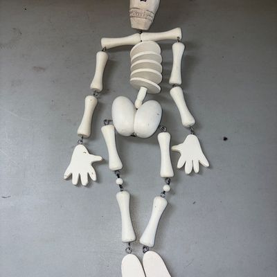 Sale Photo Thumbnail #358: Articulated wooden skeleton hanging decoration featuring jointed limbs connected by metal eye hooks and a twine loop for hanging. painted off-white with carved facial details. In good condition with light surface wear.
21in tall