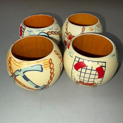 Sale Photo Thumbnail #71: A set of four rounded wooden napkin rings featuring hand-painted nautical motifs including anchors, chains, stars, and life preservers. Cream-colored exterior with natural wood interior. Minor surface wear and faint scuffs consistent with age and gentle u